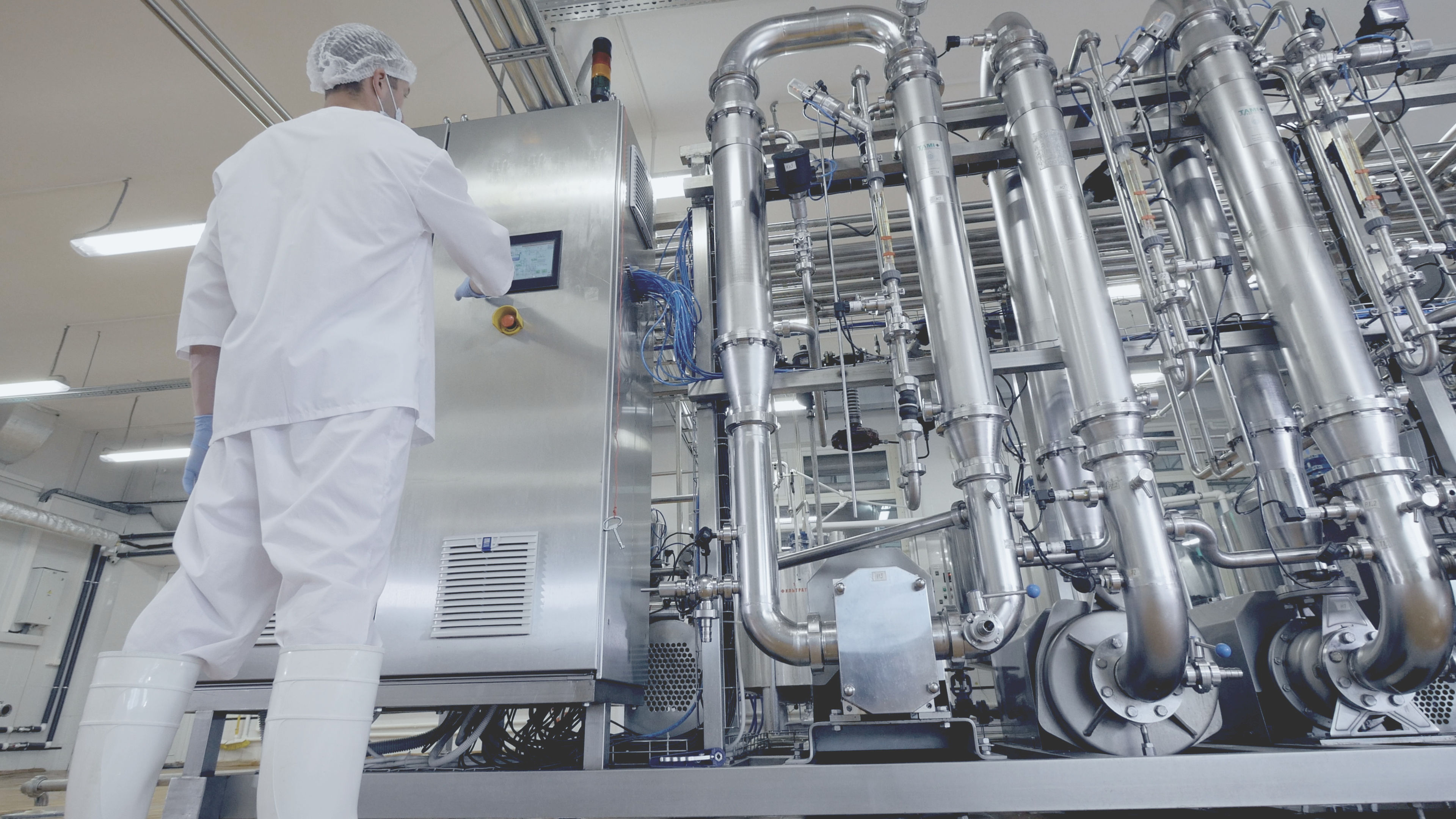 Telas sensíveis ao toque como interface de usuário no setor de processamento de alimentos Um homem com uma túnica branca e luvas brancas trabalhando em uma fábrica