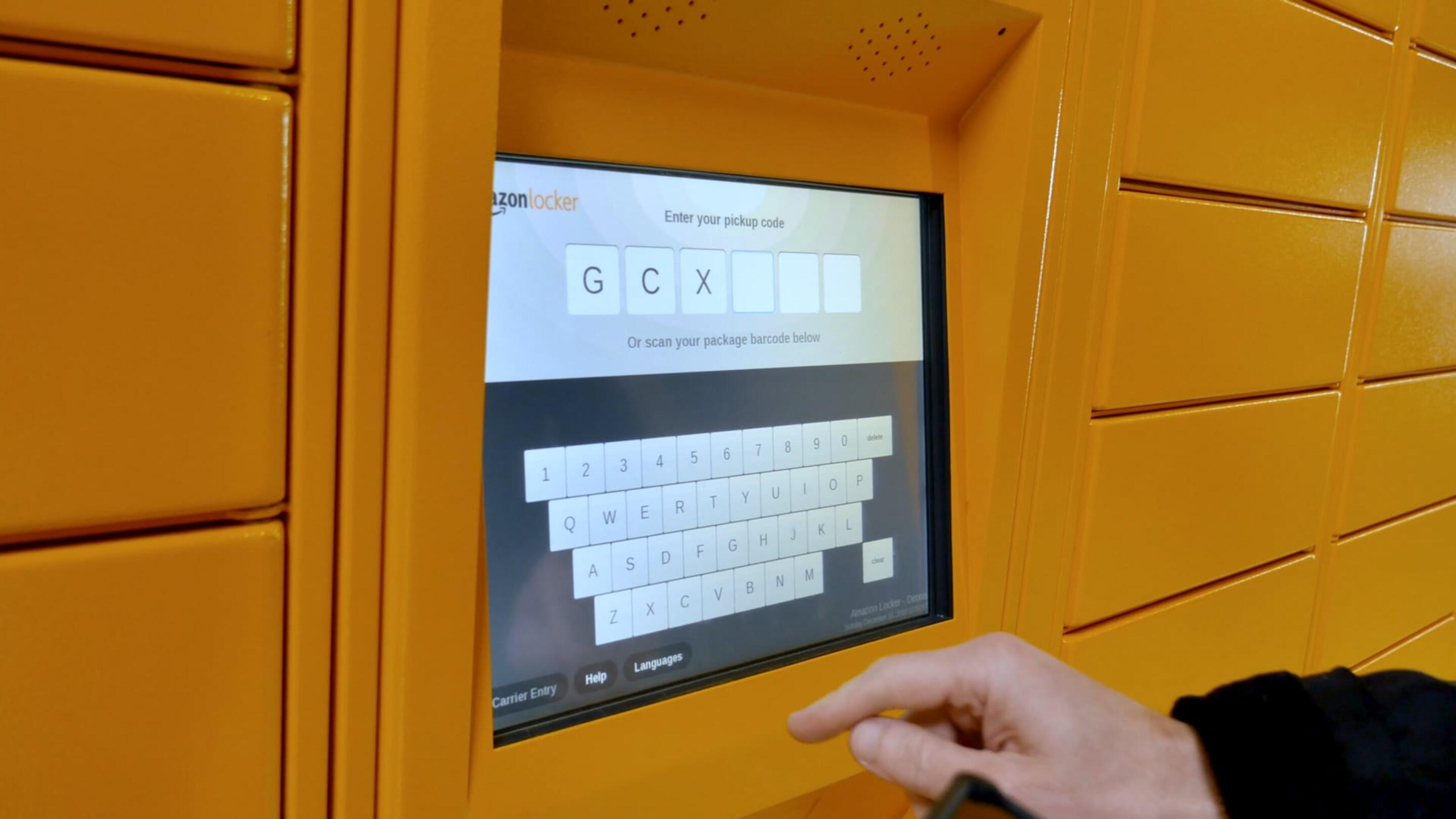 IK10 मॉनिटर - IK10 मॉनिटर टचस्क्रीन पार्सल स्टेशन एक पीले रंग की मशीन पर कीबोर्ड को छूने वाला हाथ